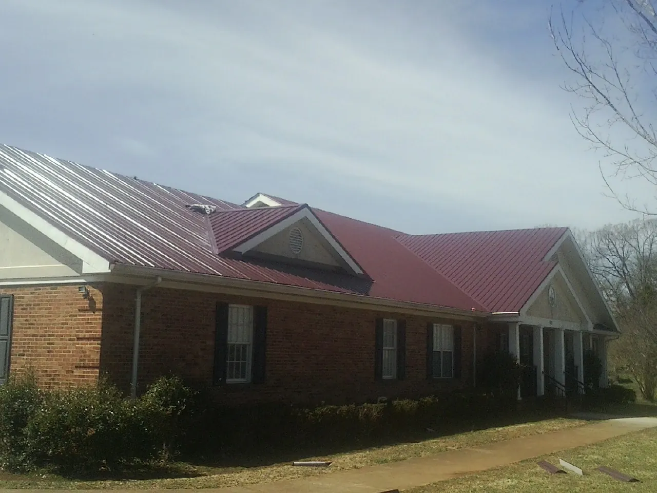 Red metal roof with gabled entries on a long brick building, from a Hail Damage Roof Repair job in San Pedro